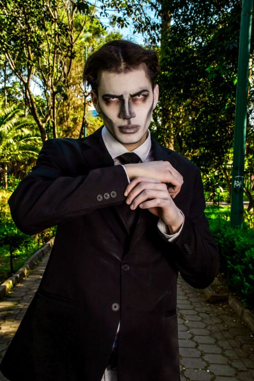 Free A man with striking gothic makeup poses stylishly in a suit in a park setting. Stock Photo