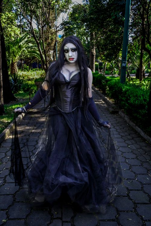 Free A gothic woman in a dark dress poses in a lush green park setting. Stock Photo