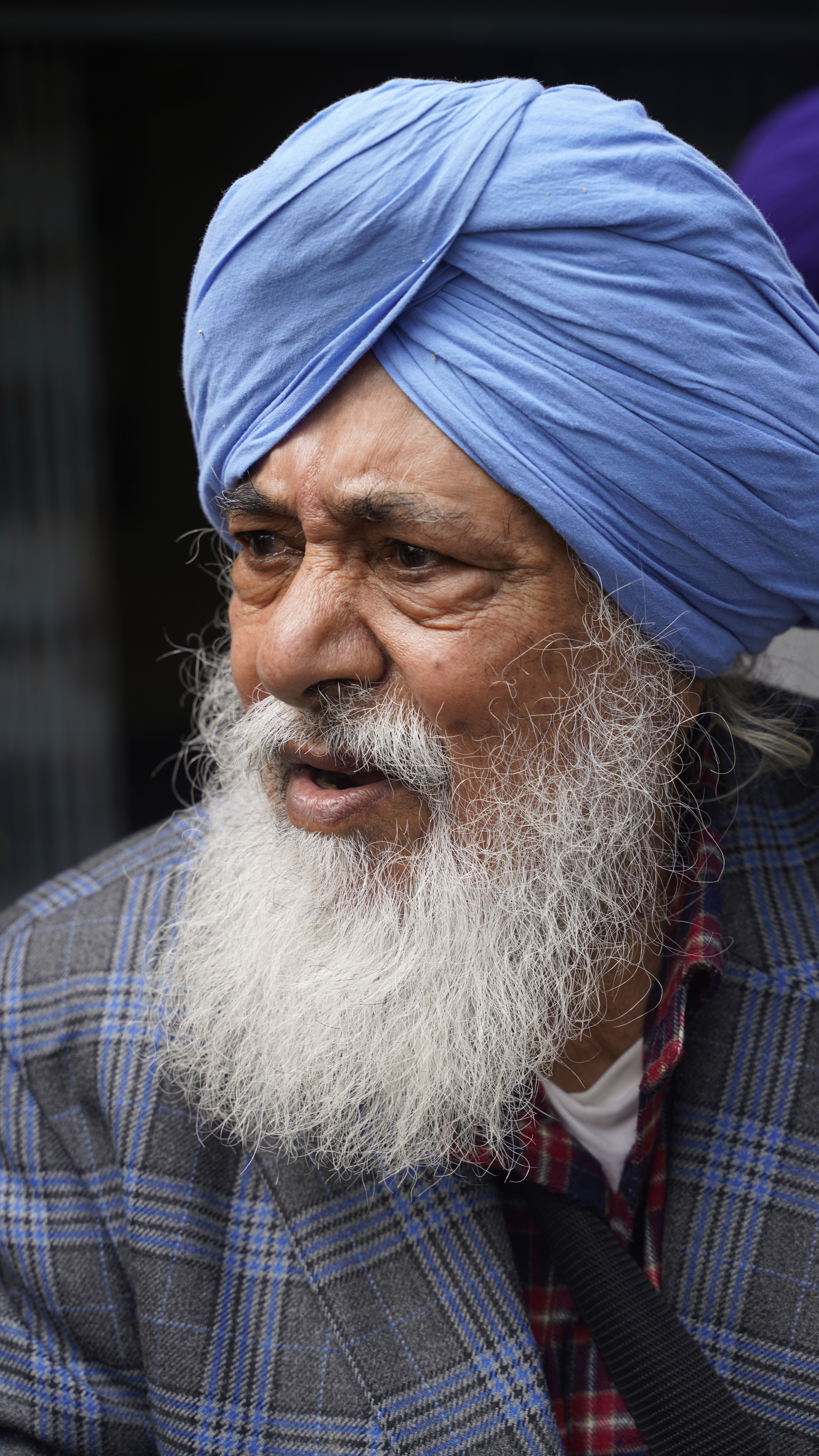 Portrait of an elderly man wearing a blue turban and plaid jacket, showcasing cultural attire and expression.