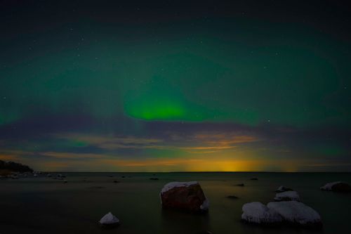 Free Beautiful aurora borealis lights the night sky over a serene, snowy coastline with icy rocks. Stock Photo