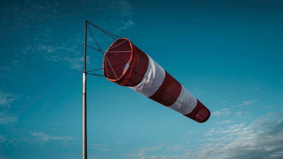 A red and white windsock on a pole against a clear blue sky on a windy day.