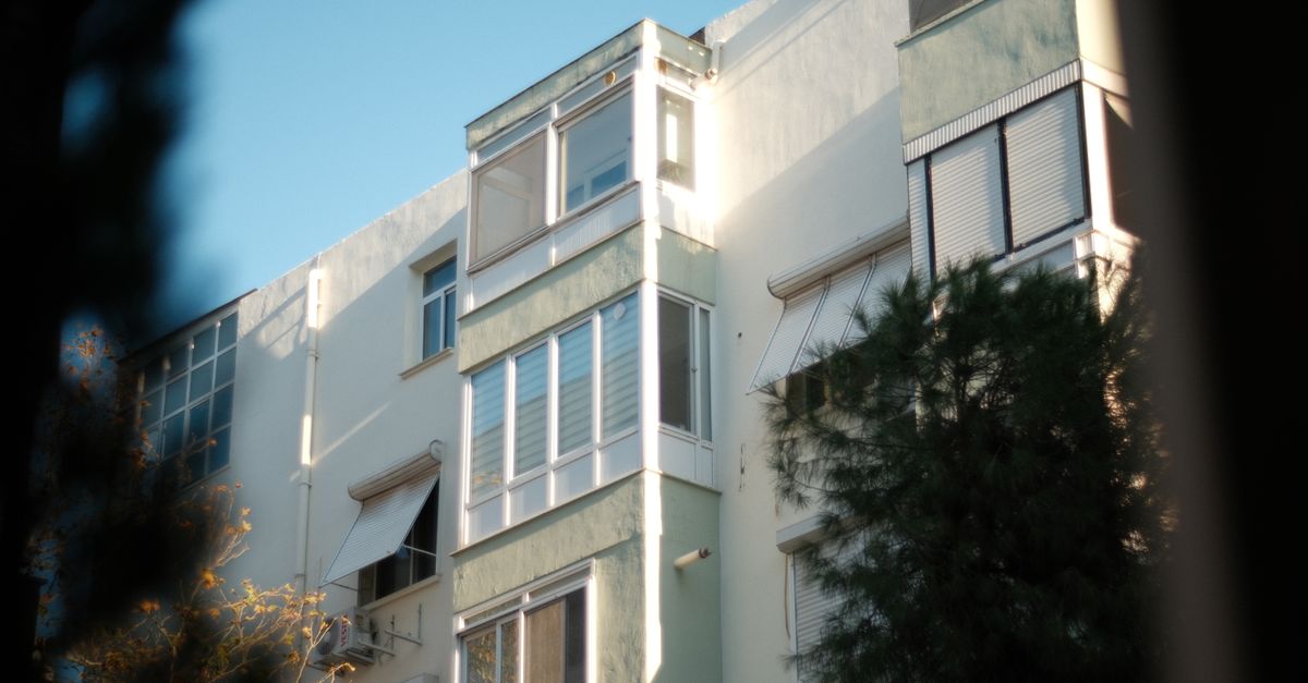 Sunlit facade of a modern apartment building with green accents and trees.