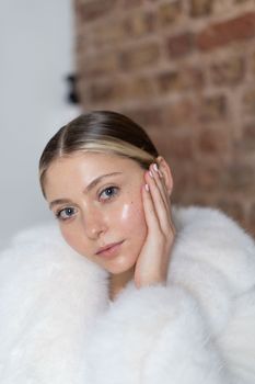Sophisticated portrait of a woman in a white fur coat against a brick wall.