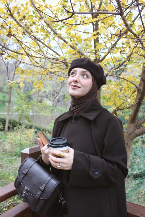 Free A young woman in autumn attire enjoys coffee in a park under yellow-leaved trees. Stock Photo