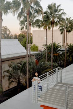 日落时分，一名妇女站在阳台上，四周环绕着郁郁葱葱的棕榈树