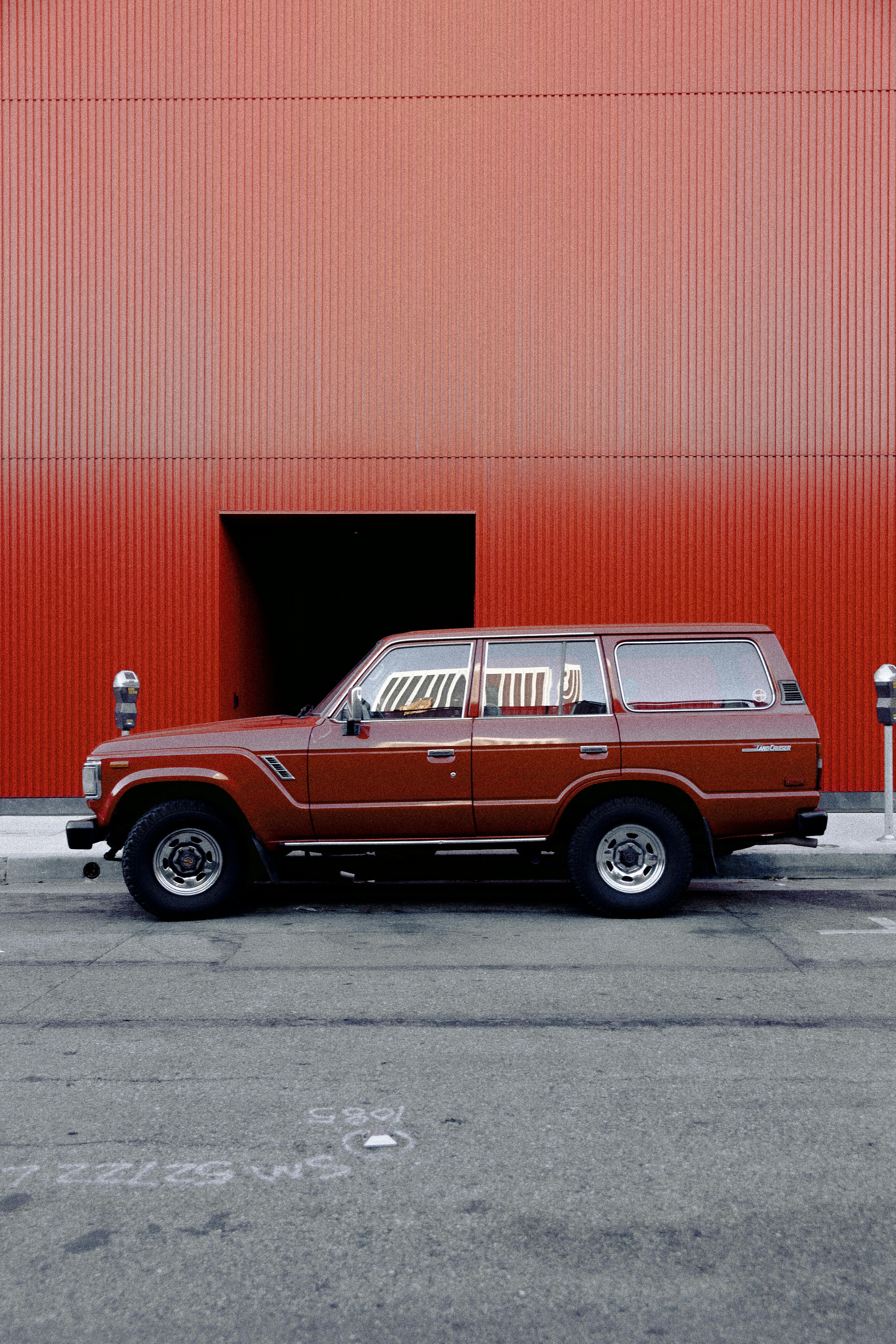 Side view of a classic Toyota Land Cruiser parked on a street beside a vibrant red wall.