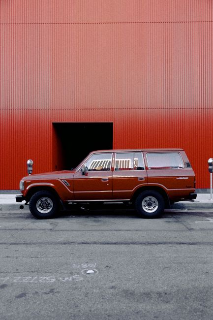 Side view of a classic Toyota Land Cruiser parked on a street beside a vibrant red wall.
