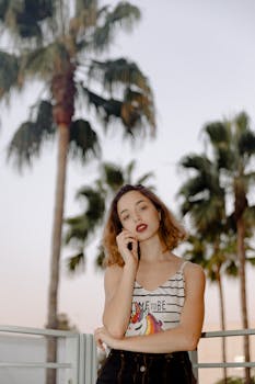 日落时分，一位别致的年轻女子倚着棕榈树，摆姿势拍摄时尚照片