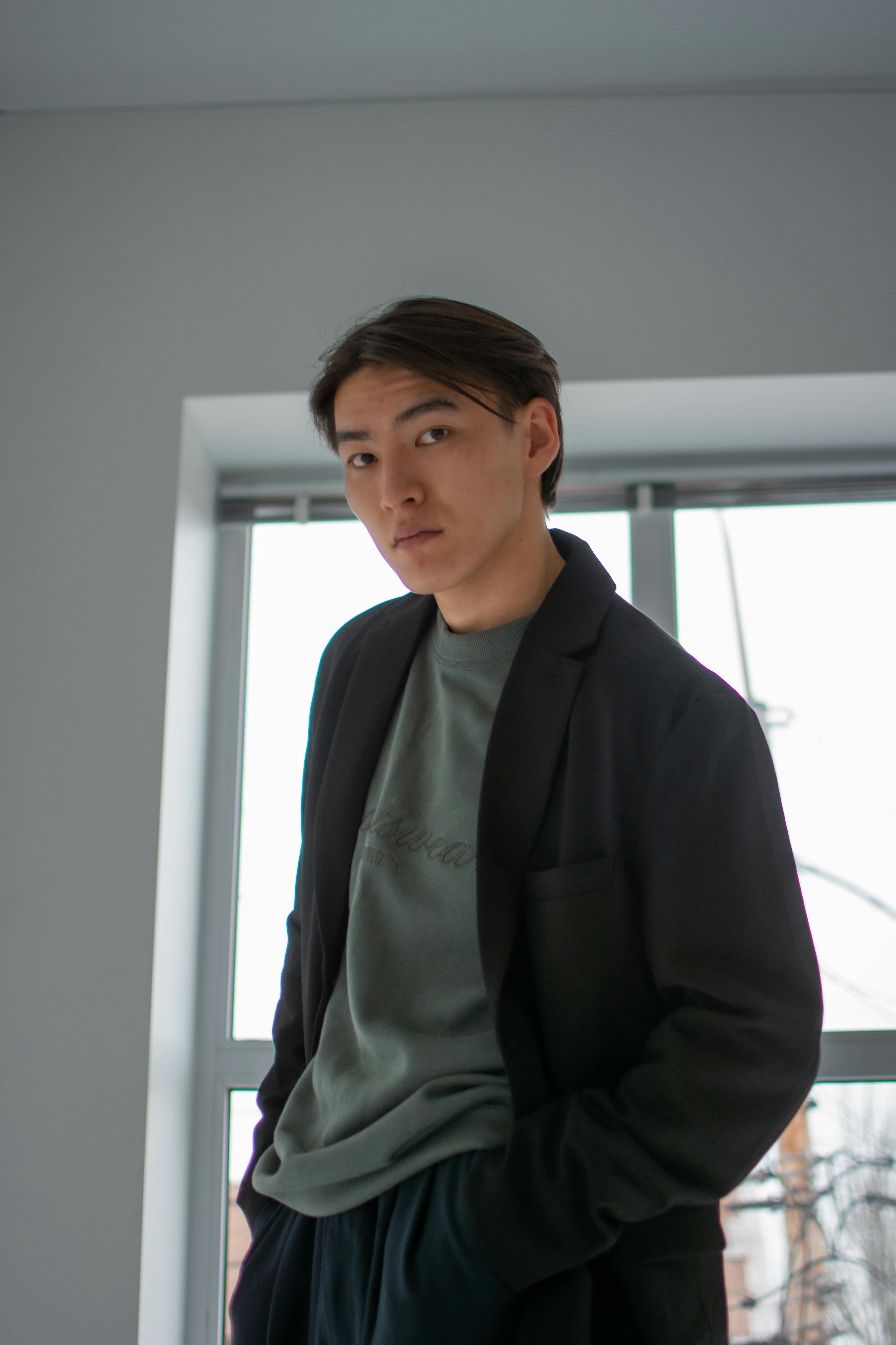 Young man in casual wear stands indoors with thoughtful expression.