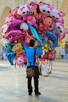 A vibrant assortment of character balloons held by a vendor at an outdoor market, attracting attention.