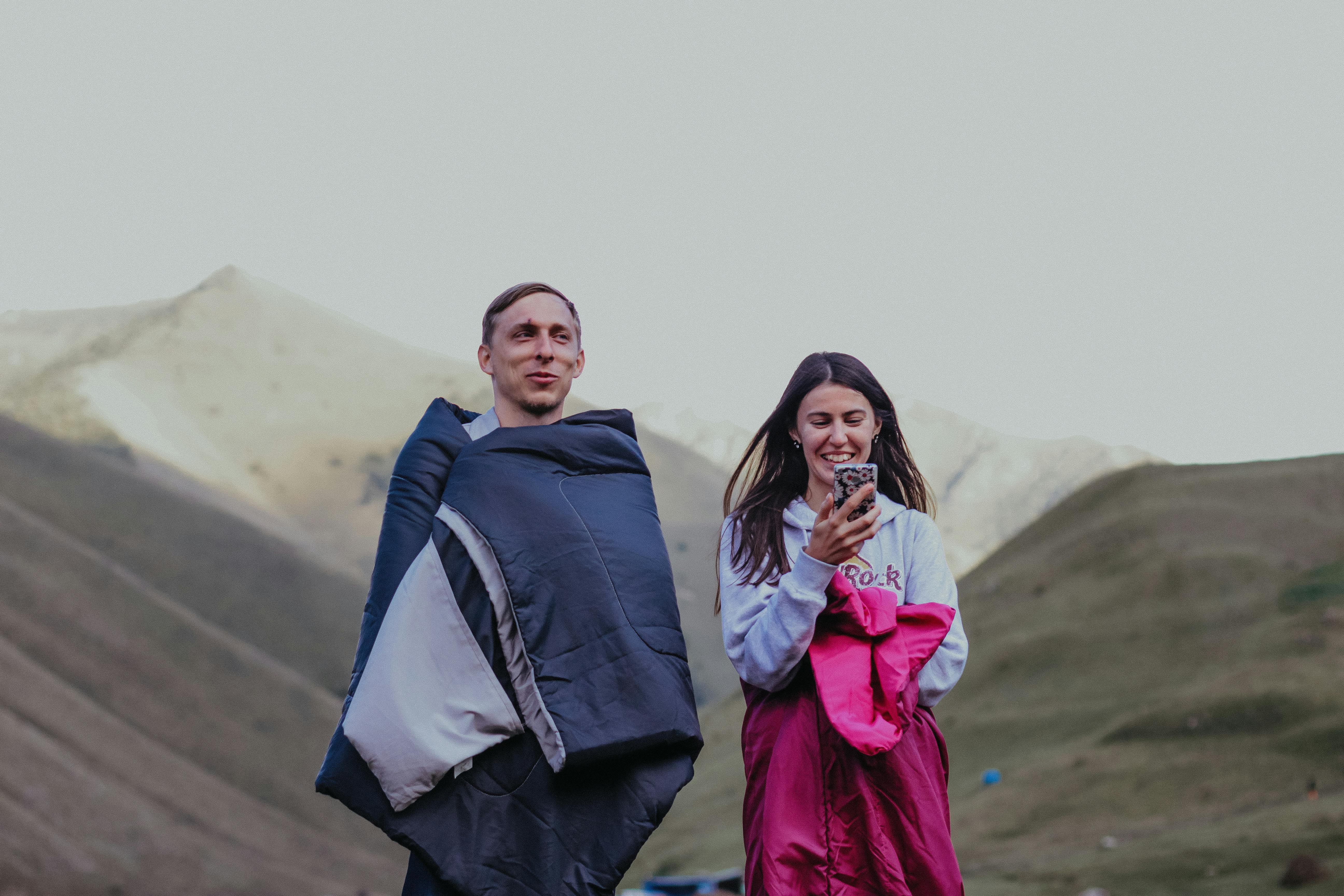 一对男女裹在睡袋里，在山区地形中享受自然和户外露营