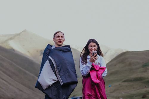 Free A man and woman wrapped in sleeping bags enjoying nature and outdoor camping in mountainous terrain. Stock Photo