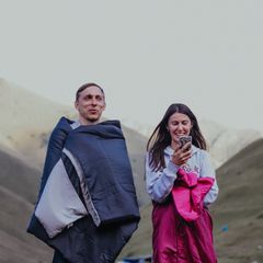 Two friends wrapped in navy and pink sleeping bags in the hills