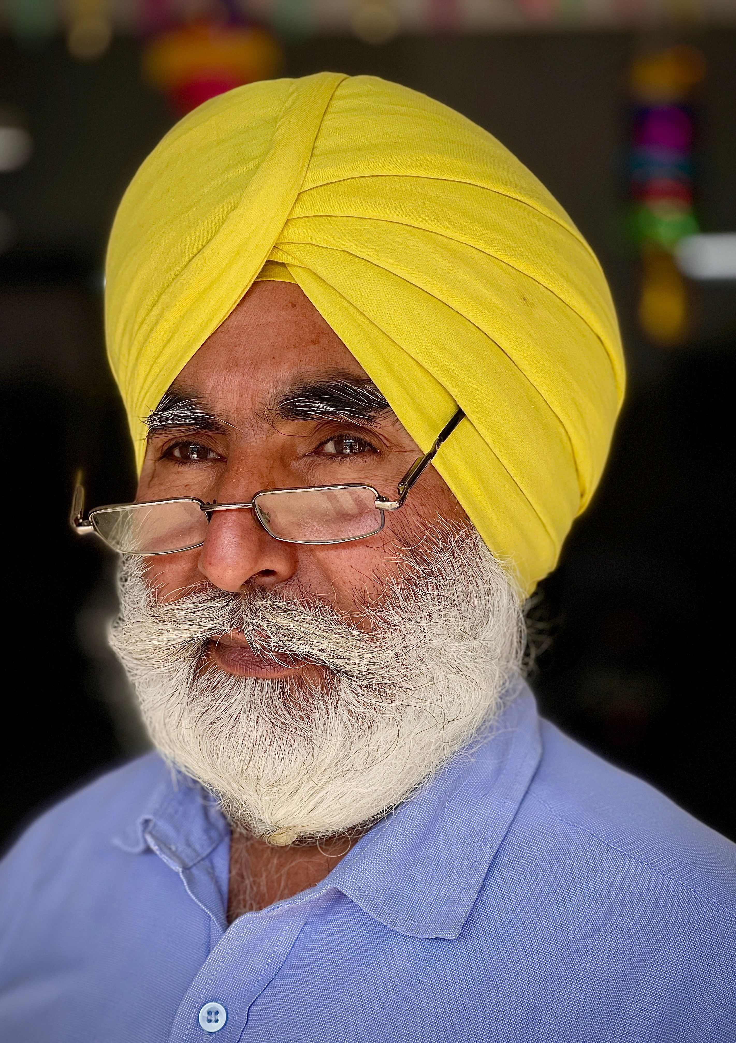A distinguished man wearing a yellow turban and glasses, exuding wisdom and warmth.