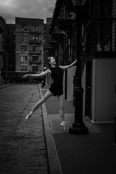 A poised ballerina performs an elegant dance pose on a dimly lit urban street.