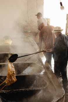 Men work in artisan sugar production, stirring hot syrup in large pots indoors.