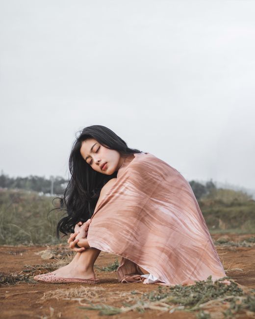 Woman sitting outdoors wrapped in shawl, exuding calm and serenity against a natural backdrop.
