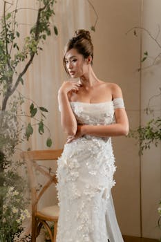 A beautiful bride in a lace wedding dress poses indoors with elegant floral decor.