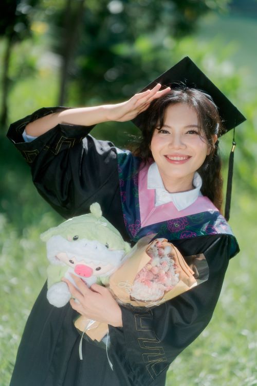 Free Cheerful graduate posing with cap, gown, and bouquet, celebrating success. Stock Photo