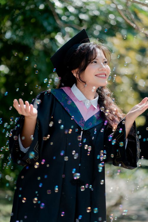 Free Young woman celebrating graduation outdoors with bubbles floating around. Stock Photo