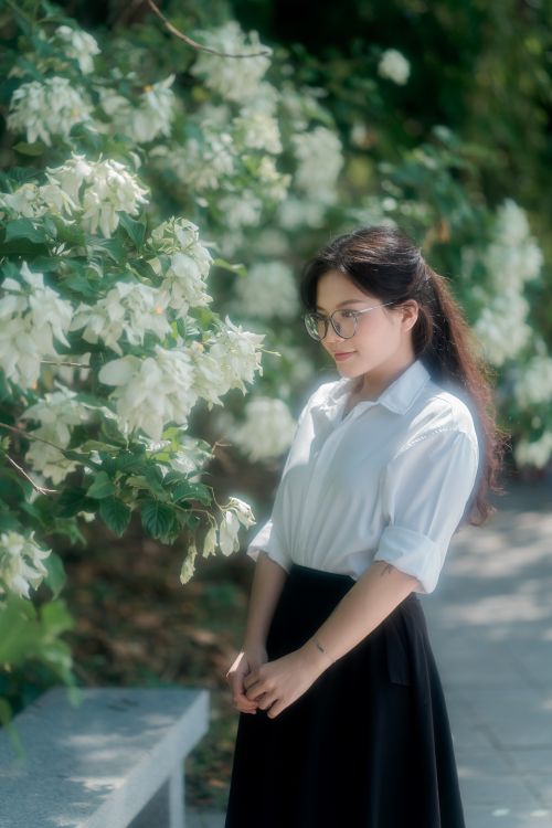 Free Adult woman in glasses enjoying the beauty of a blossoming tree in a sunlit garden setting. Stock Photo