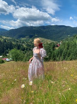 Blonde woman in floral dress exploring a meadow in the Carpathians during summer.