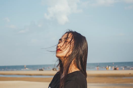 A woman enjoying a tranquil moment at the beach with a windy sea breeze under clear skies.
