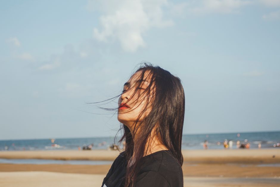 A woman enjoying a tranquil moment at the beach with a windy sea breeze under clear skies.