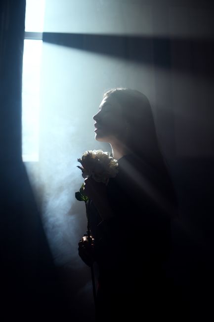 Silhouette of a woman holding peonies with dramatic lighting from window.
