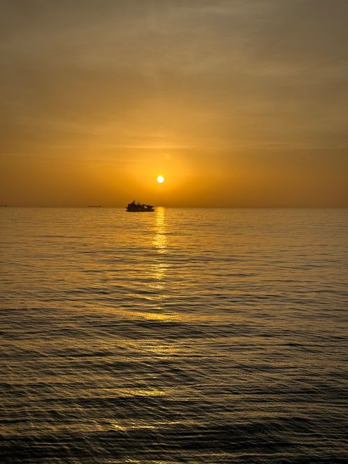 Free A serene sunset view over calm ocean waters with a distant silhouette of a boat. Stock Photo