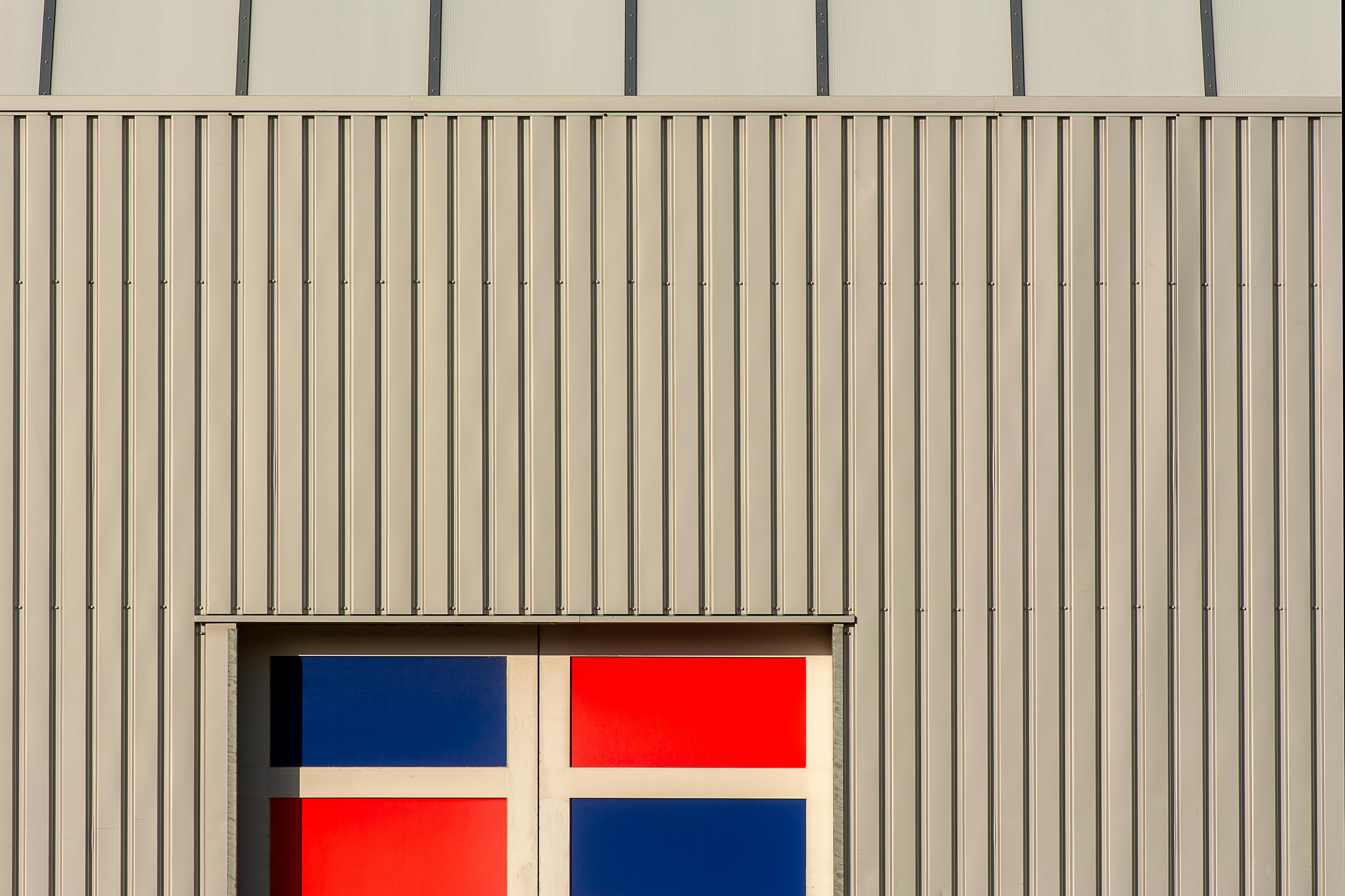Gratuit Façade de bâtiment contemporain avec un design géométrique coloré comportant des panneaux rouges et bleus. Photos