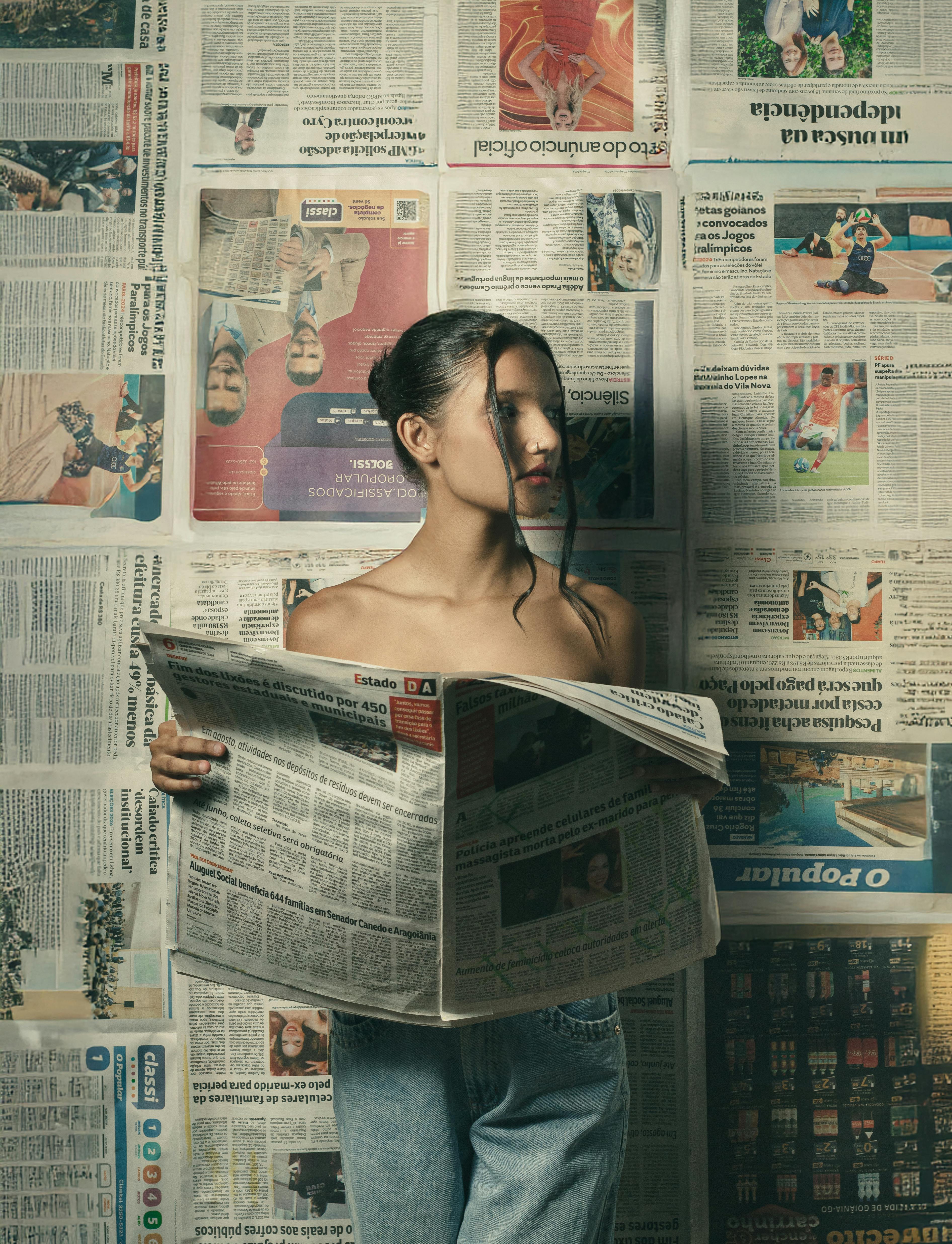 A woman reads a newspaper against a wall covered in newsprints, creating an artistic and moody atmosphere.