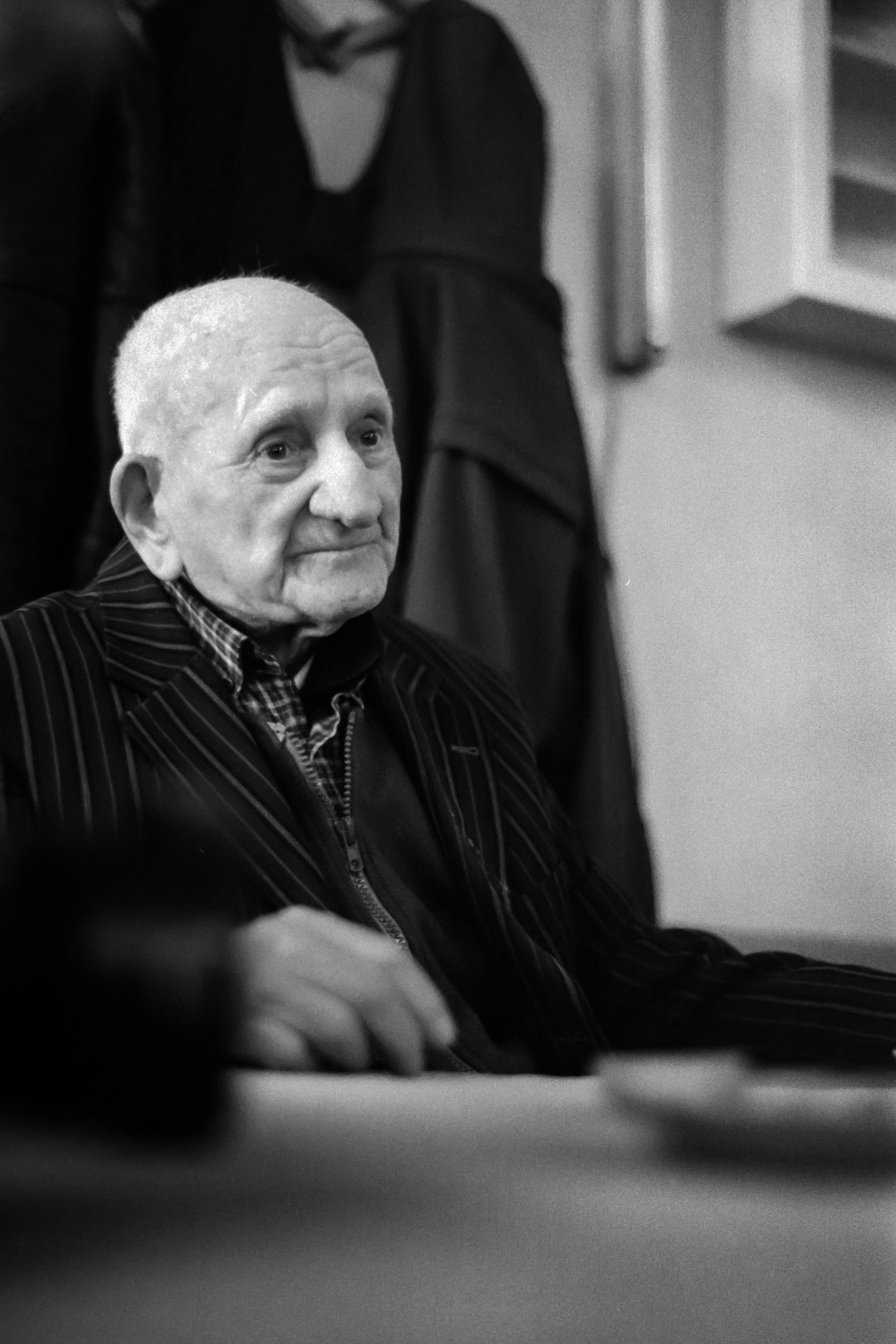 Elegant black and white portrait of an elderly man in a striped suit sitting indoors.
