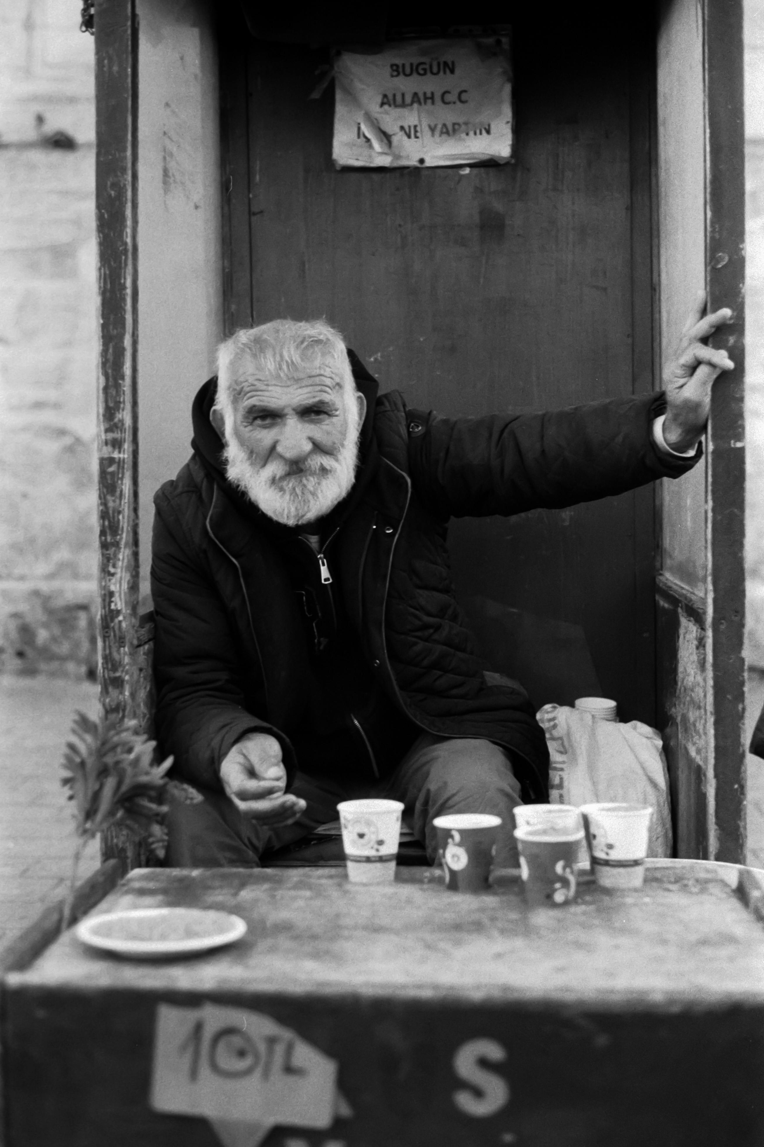 Black and white portrait of an elderly man with coffee cups in Istanbul, Türkiye.