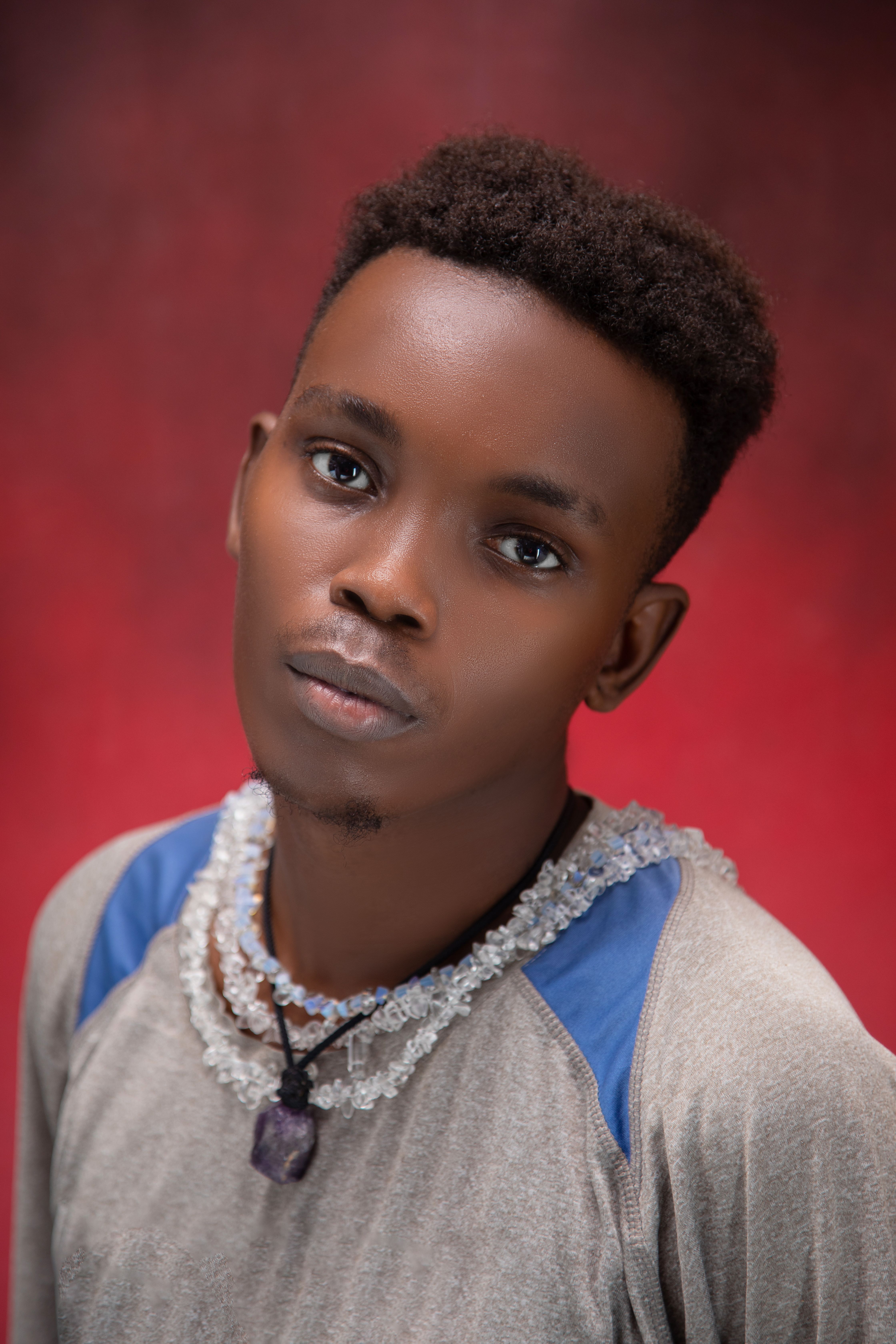 Studio portrait of a young man wearing necklaces and a stylish shirt against a red background.
