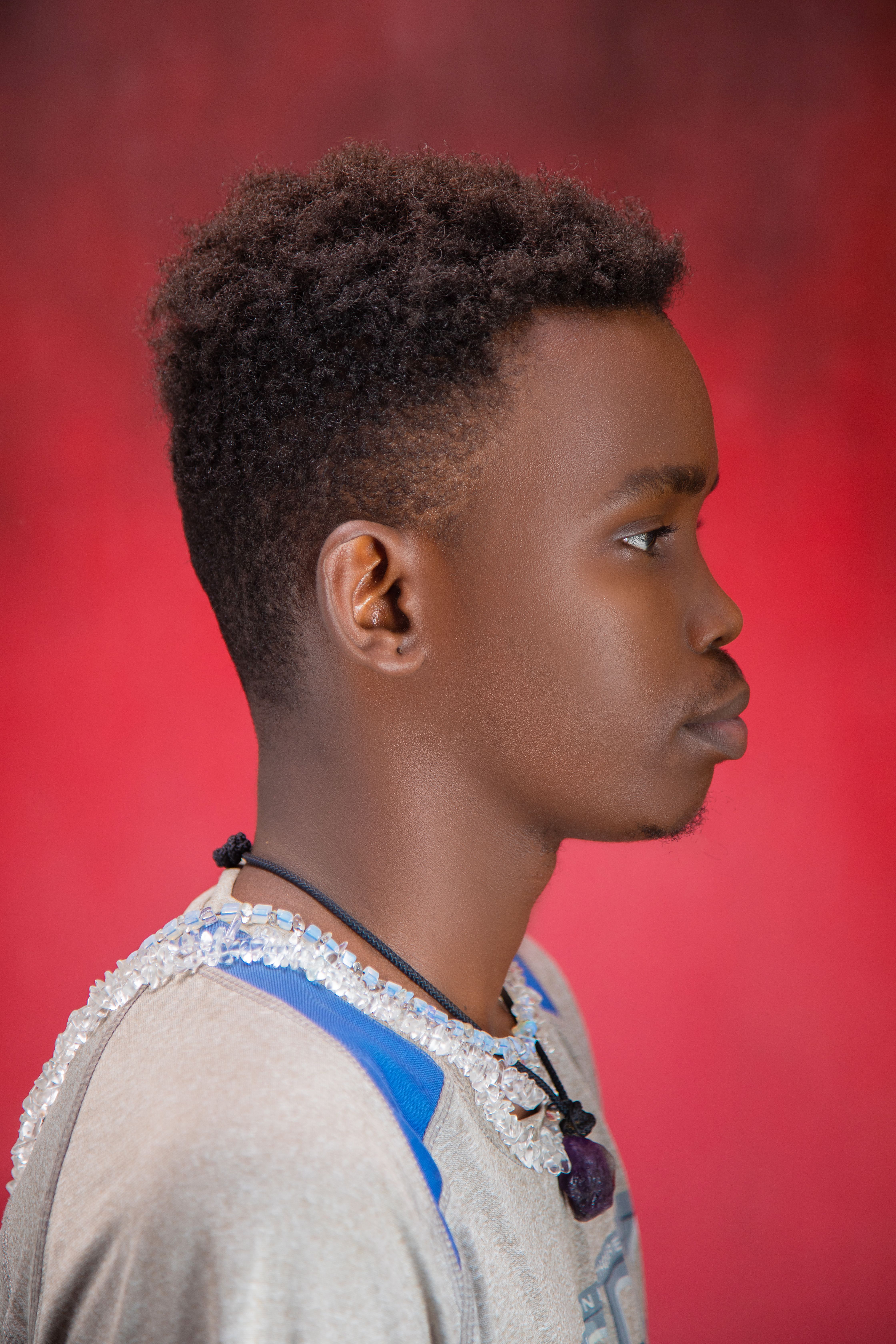 Side profile portrait of a young man against a vibrant red backdrop.