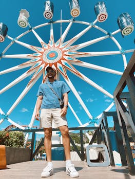 A man standing in front of a colorful Ferris wheel at a fairground in La Libertad, El Salvador. Sunny day fun.