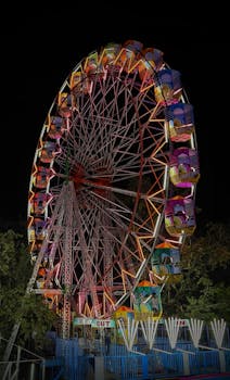 A vibrant multicolored Ferris wheel illuminating the night sky at an amusement park in Pune, India.