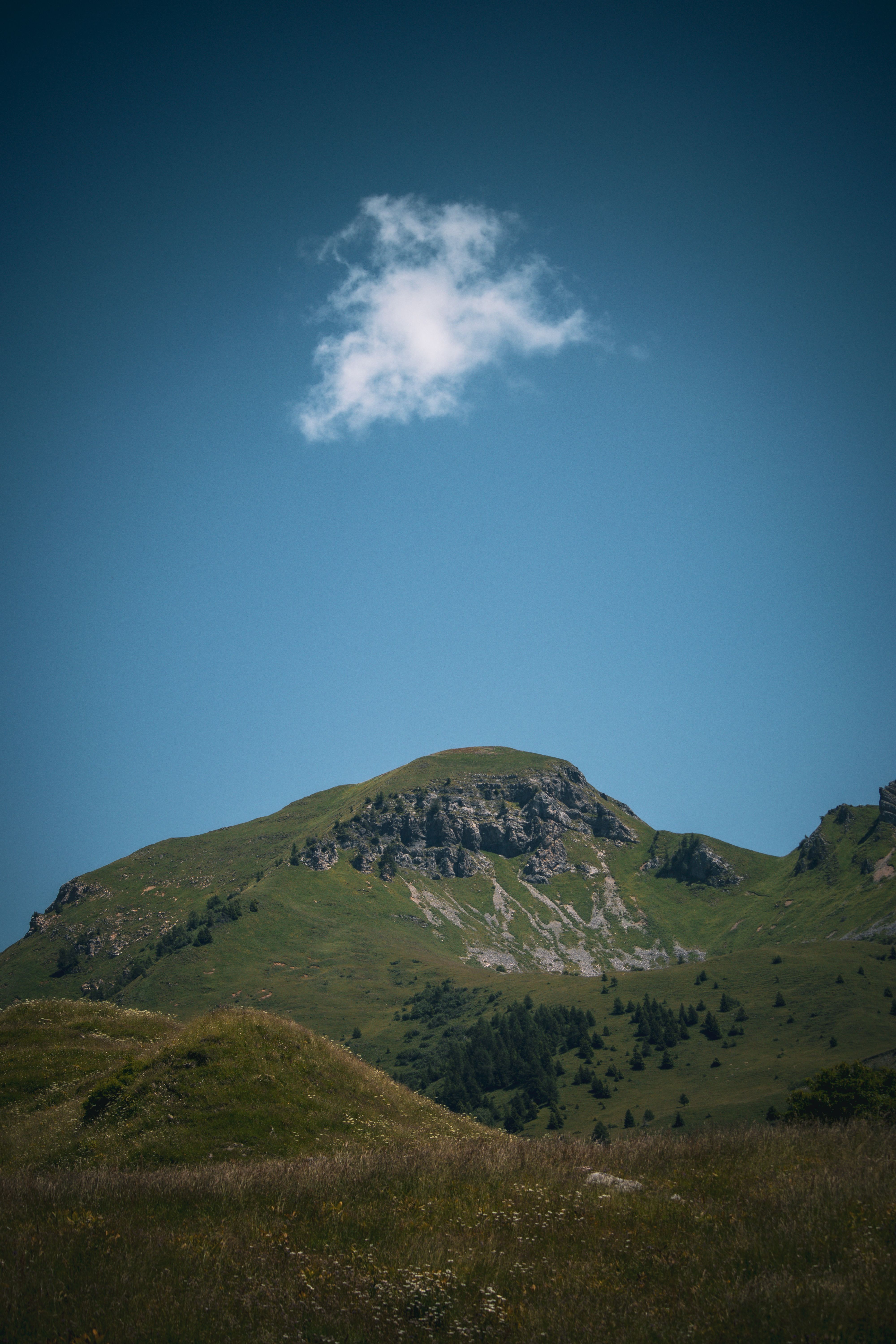 A serene view of a lush green mountain under a clear blue sky with a single cloud.