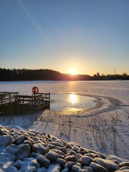 A beautiful winter sunrise over a frozen lake with a pier and rocks in the foreground.