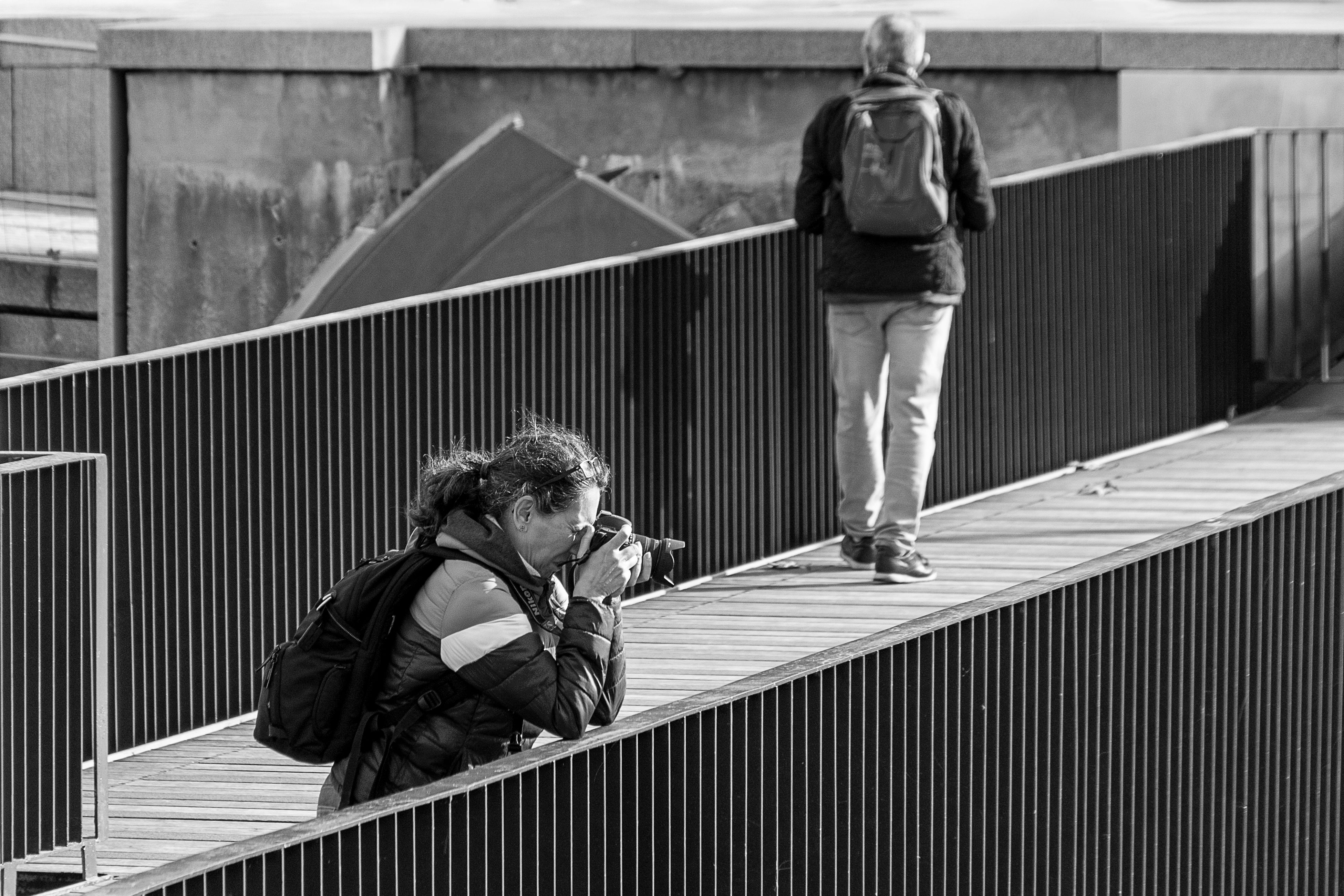Black and white photo of a photographer capturing a scene on a modern urban bridge. - Madrid