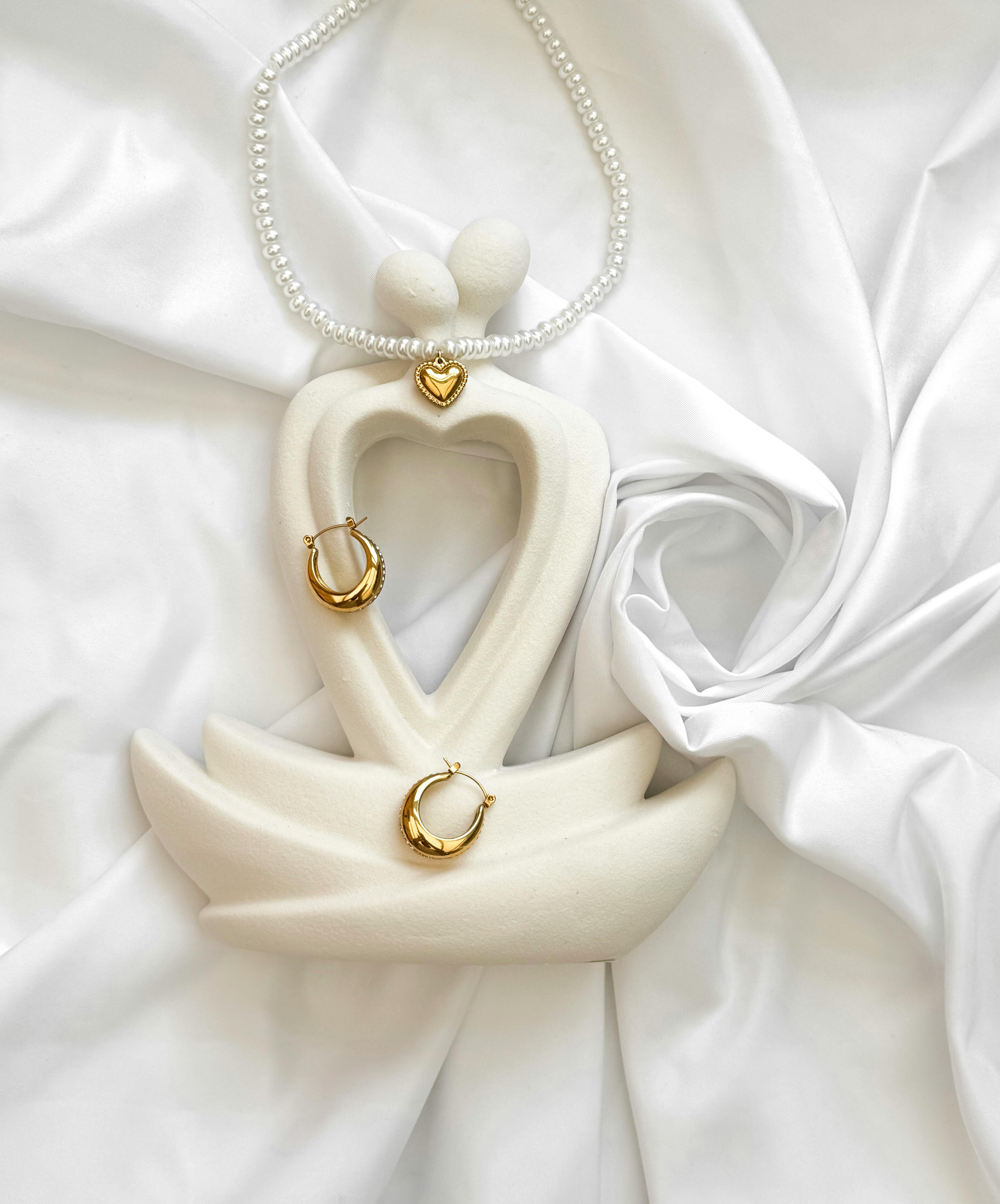 Stylized heart-shaped figurine with gold jewelry on white fabric, exuding elegance.