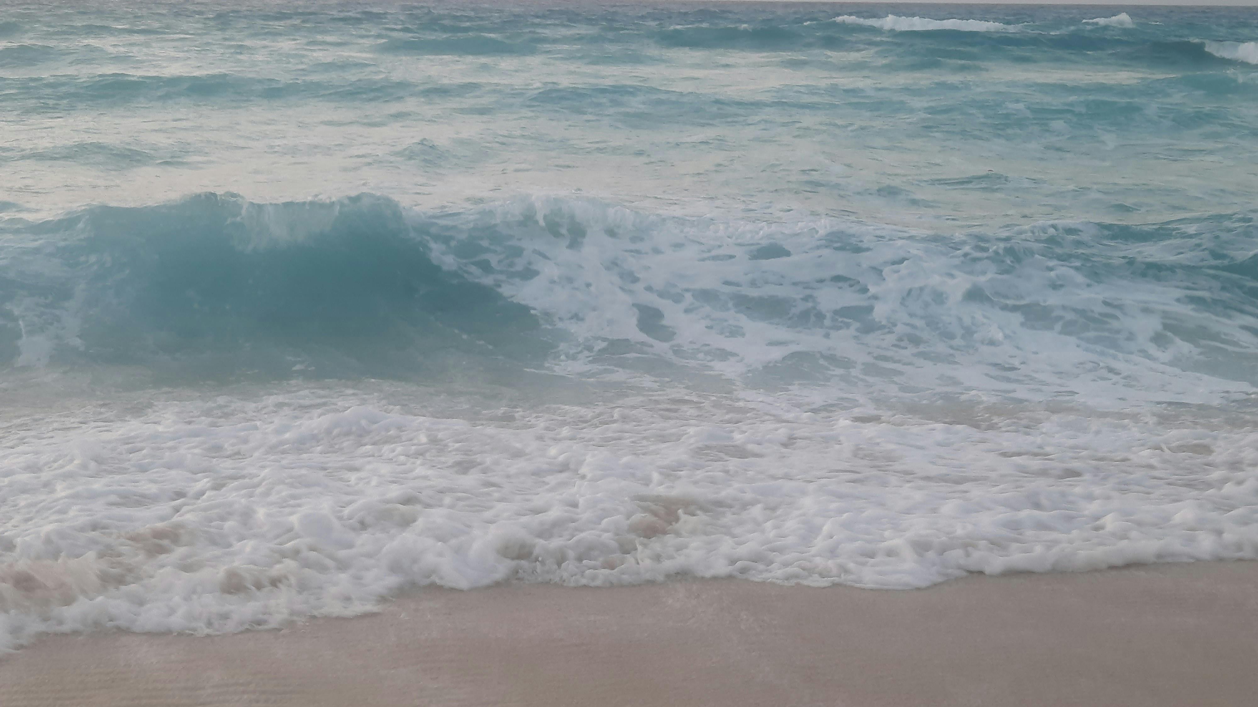 Peaceful ocean waves gently crashing on a sandy beach at daytime.