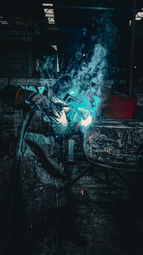 Free A skilled welder in action, creating sparks and smoke in a dark industrial environment. Stock Photo