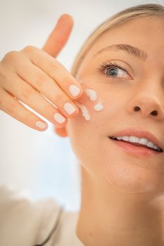 Close-up of a woman's face applying moisturizer, showcasing skincare routine and healthy skin.