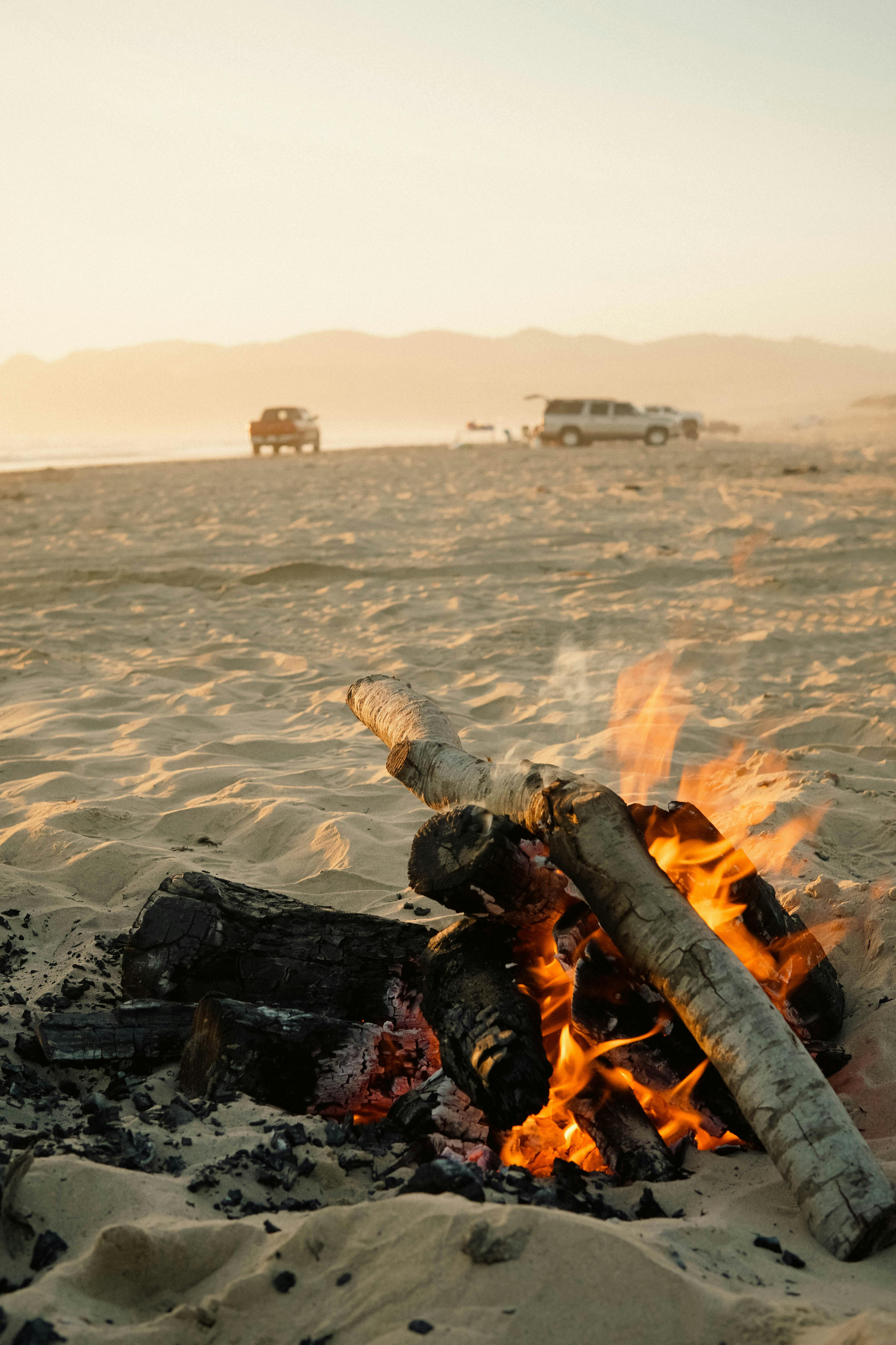 A warm bonfire on a sandy beach during sunset, creating a perfect atmosphere for a coastal evening.
