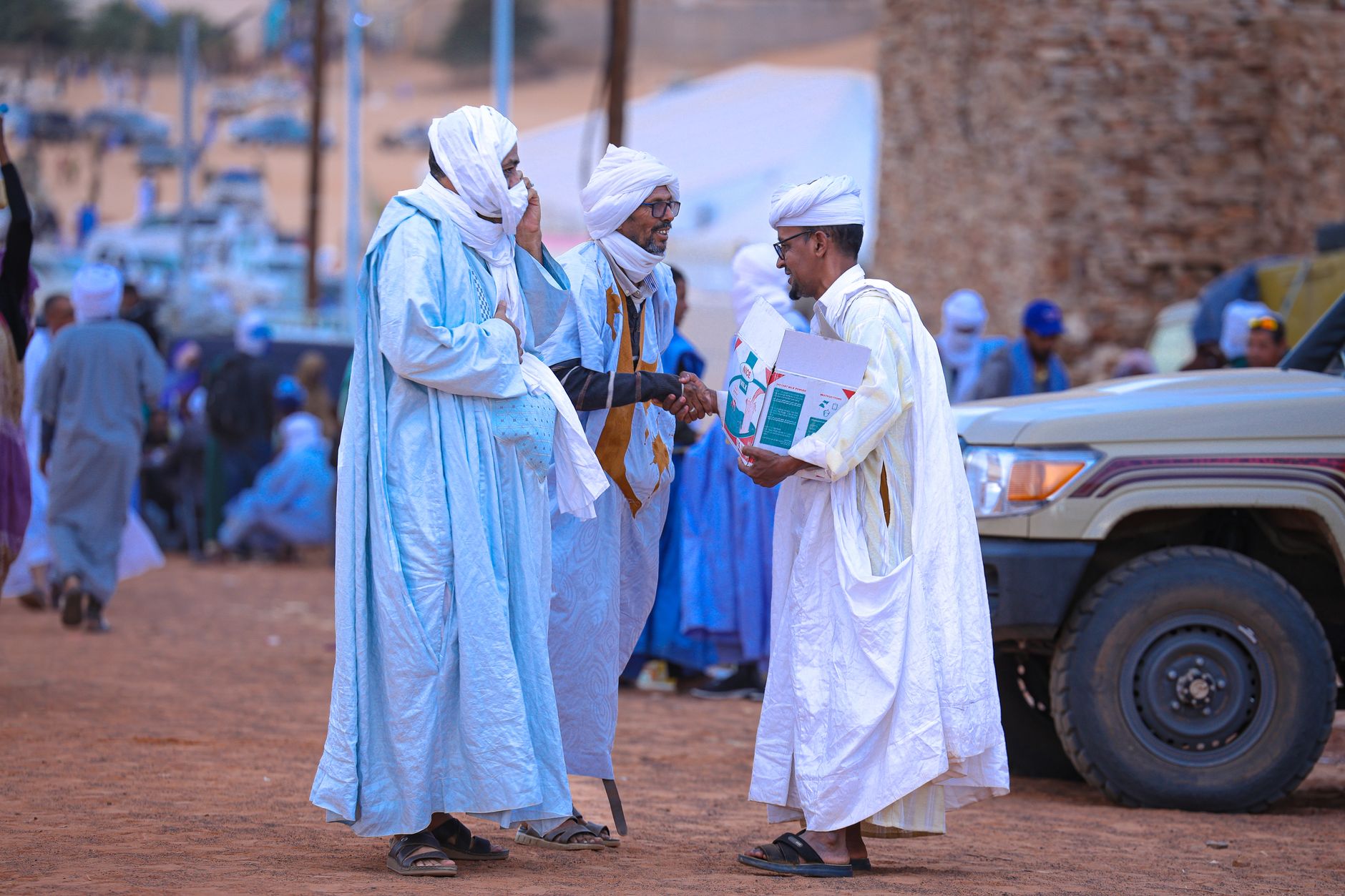 Three men in traditional Moroccan attire conversing in a bustling outdoor marketplace.