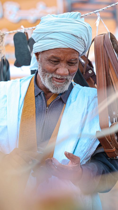 Free Elderly man in traditional clothing smiles while shopping at a vibrant outdoor market. Stock Photo