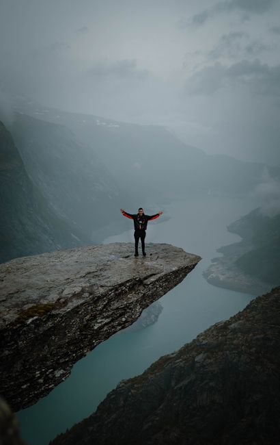 Person posing with open arms on Trolltunga cliff in Norway during a foggy day.
