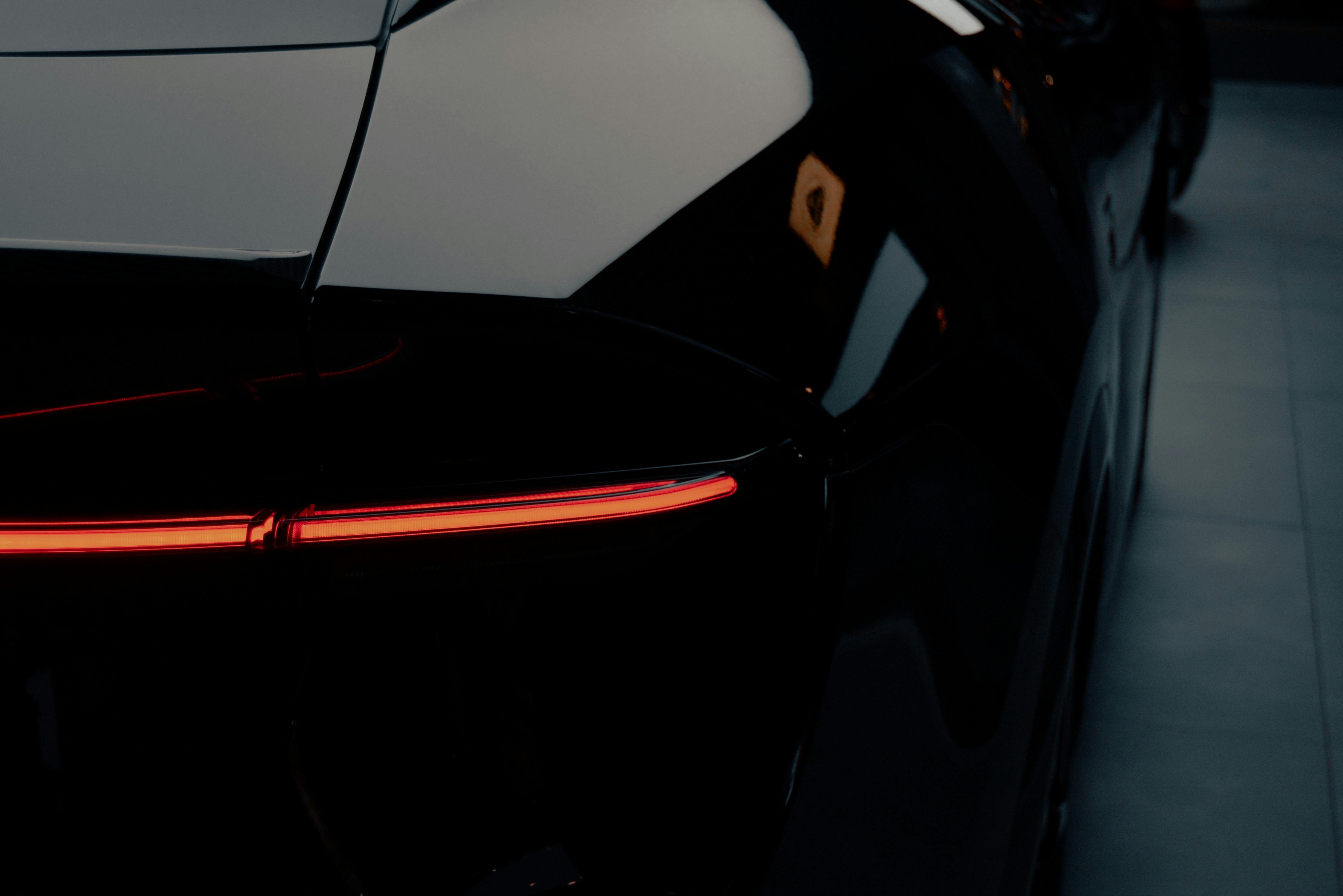 Free A close-up shot of a sleek black sports car featuring its striking red tail light design. Stock Photo